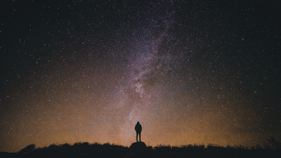Una persona mirando el cielo nocturno en el que se muestra una galaxia lejana