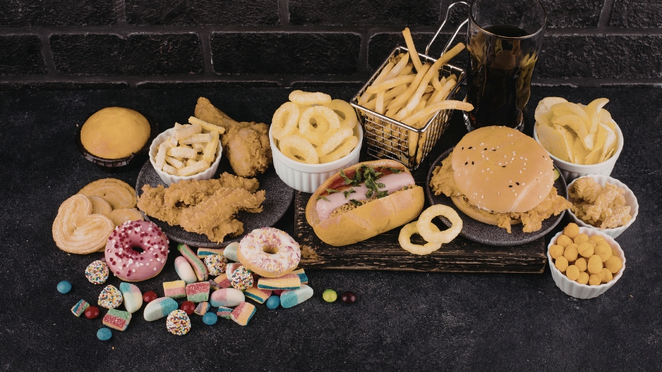 Dulces, gominolas, bollería y comida alta en calorías distribuidas por un fondo oscuro que representan el placer inmediato