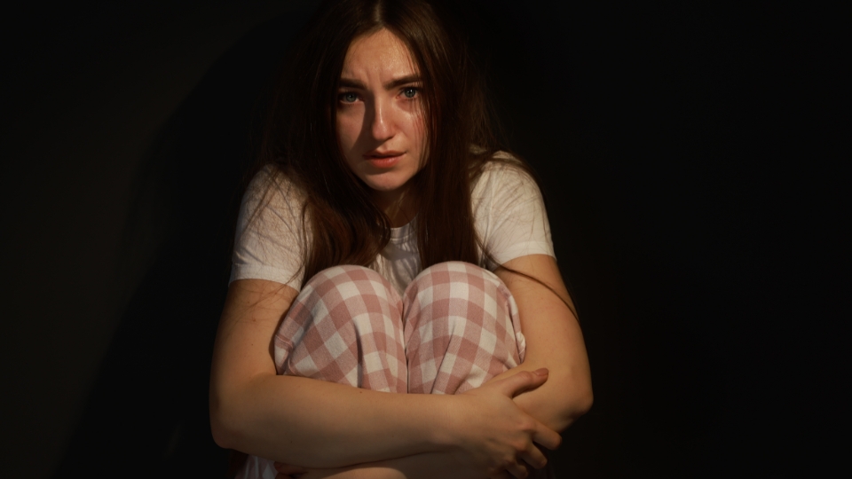 Una mujer joven cogiéndose las rodillas asustada