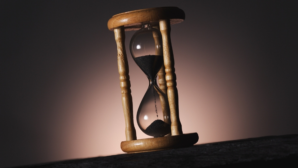 Un reloj de arena iluminado sobre un fondo oscuro con la arena cayendo representando el paso del tiempo